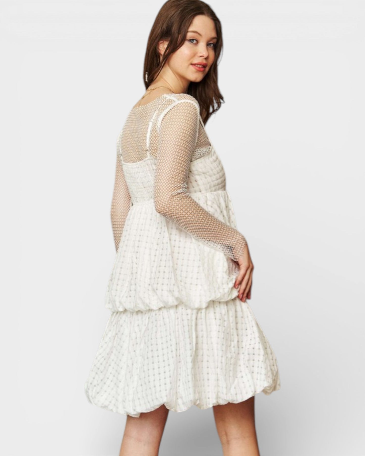 Woman wearing a white dress with sheer sleeves on a plain background