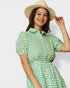 Woman wearing a green checkered dress and beige hat on a white background