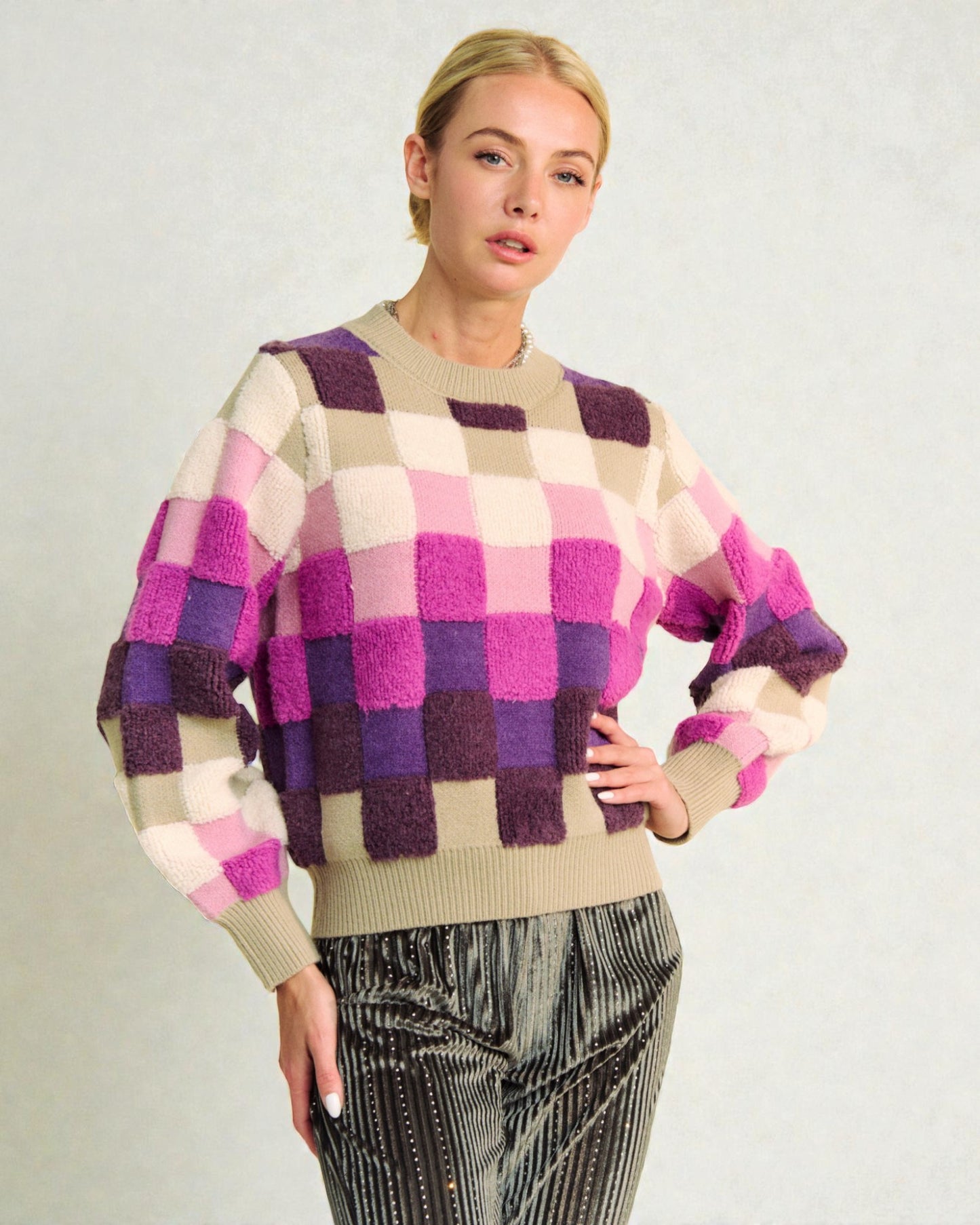 Woman wearing a checkered sweater with purple, pink, and beige colors on a plain background