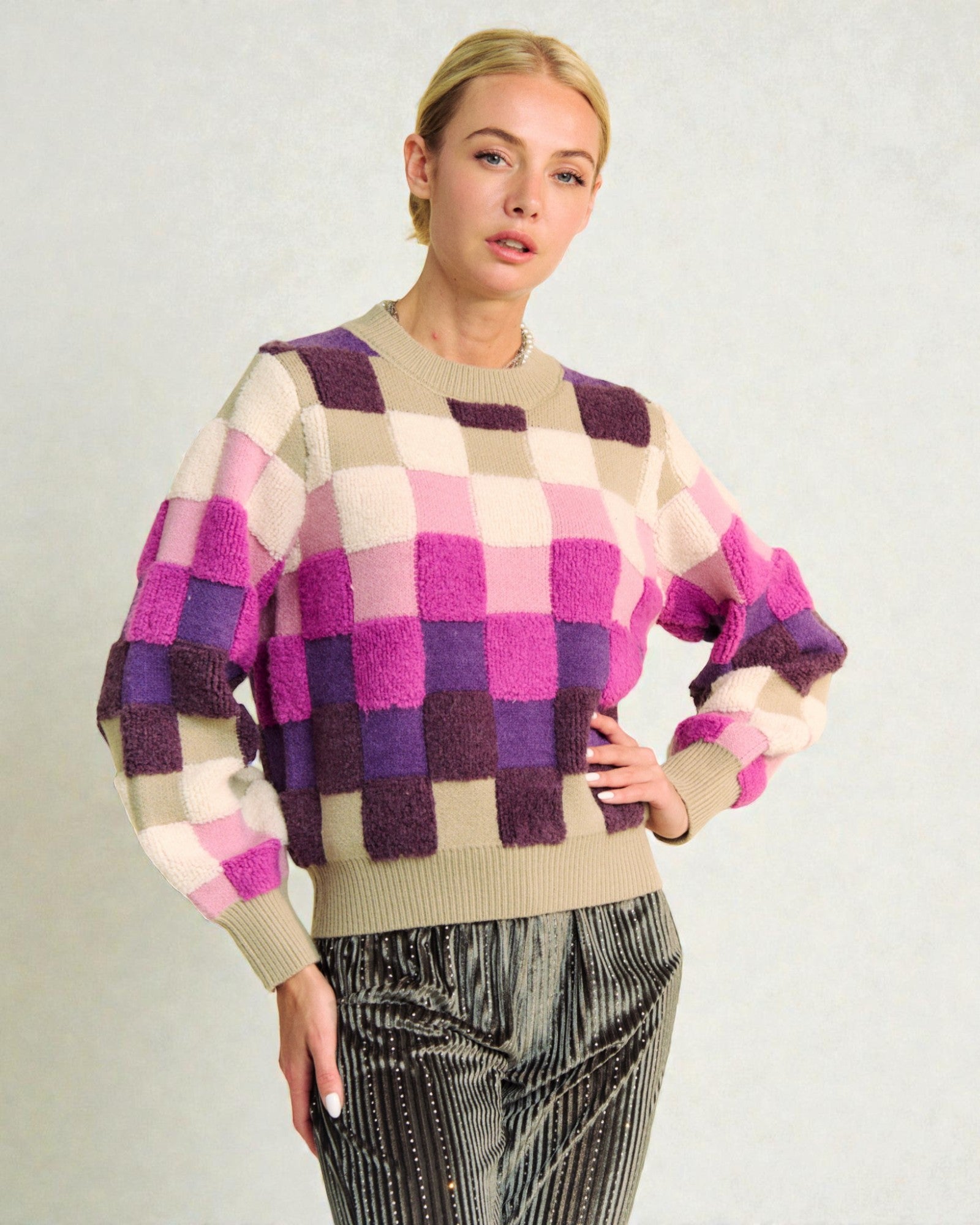 Woman wearing a checkered sweater with purple, pink, and beige colors on a plain background