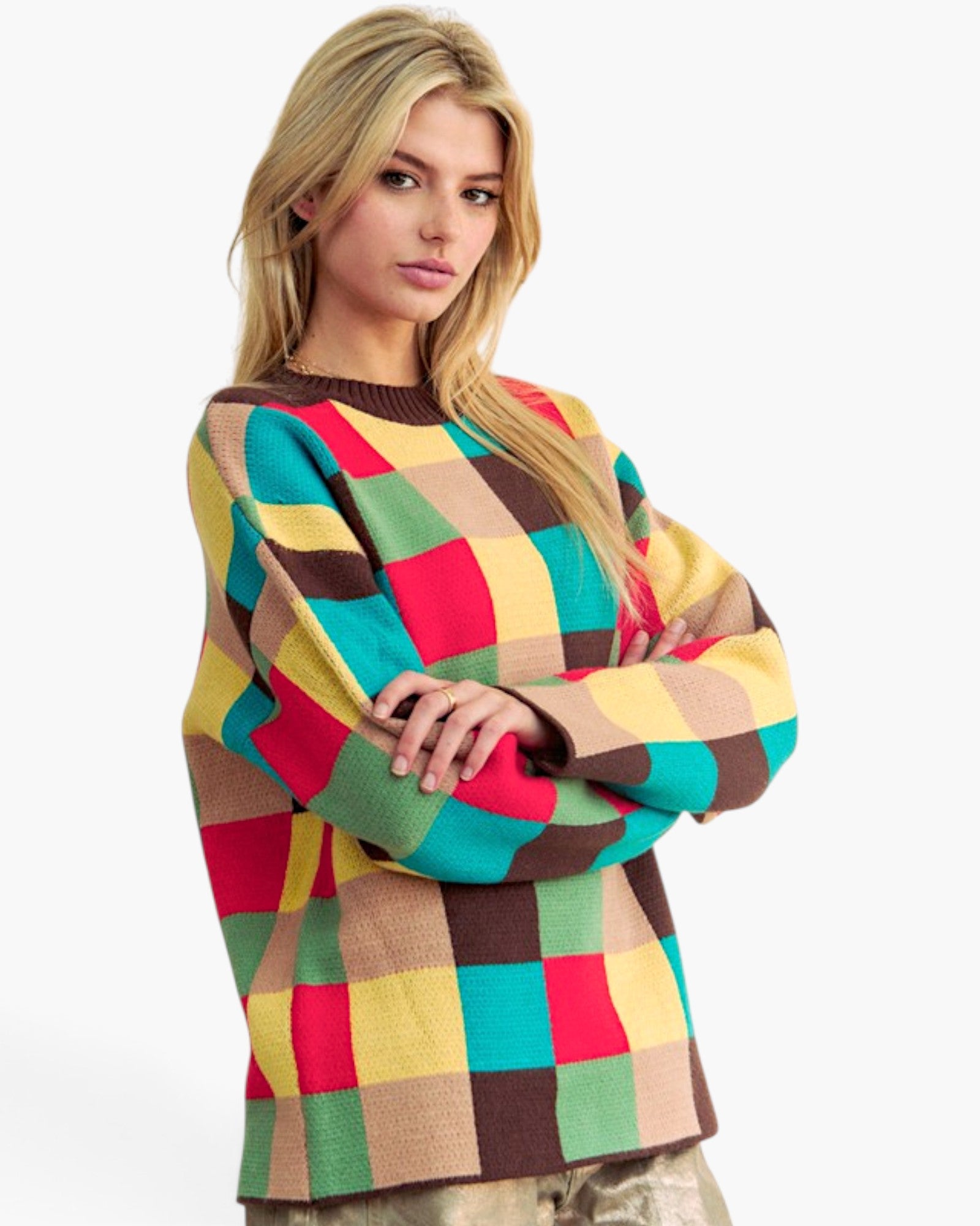 A blonde model wearing a chunky knit sweater with a large multicolor checkered pattern in red, yellow, green, brown, and beige, posed against a solid white background.