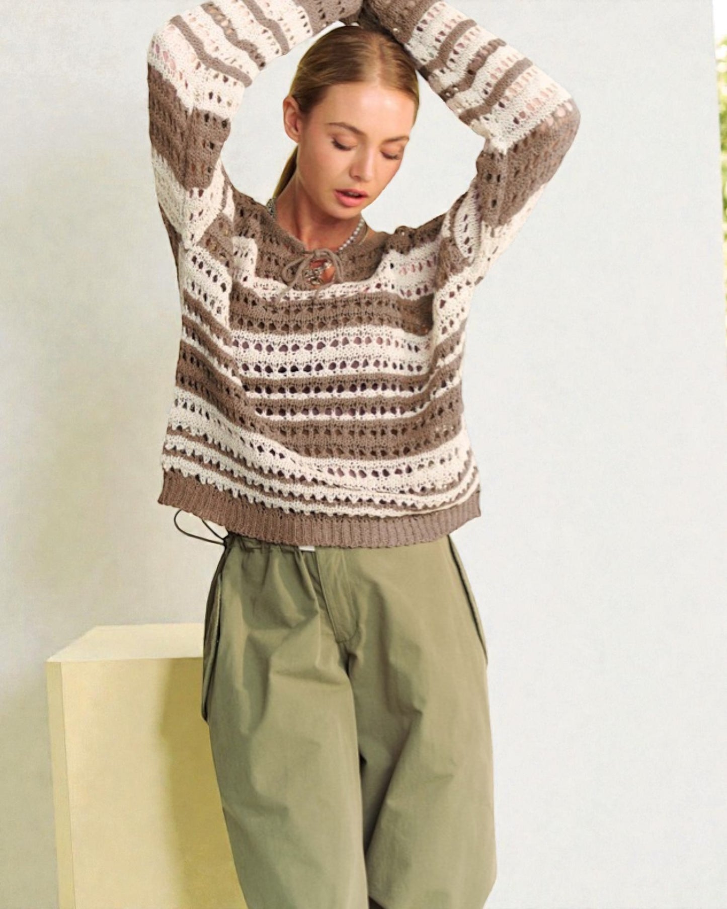 Woman wearing a patterned sweater and green pants against a light background