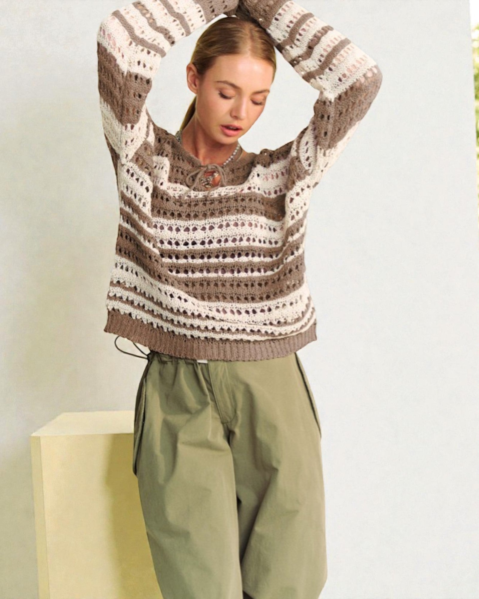 Woman wearing a patterned sweater and green pants against a light background