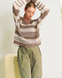 Woman wearing a patterned sweater and green pants against a light background