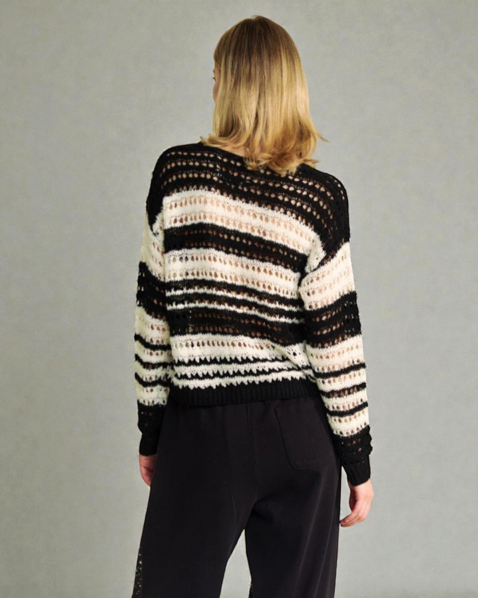 Person wearing a black, white, and beige striped sweater against a gray background