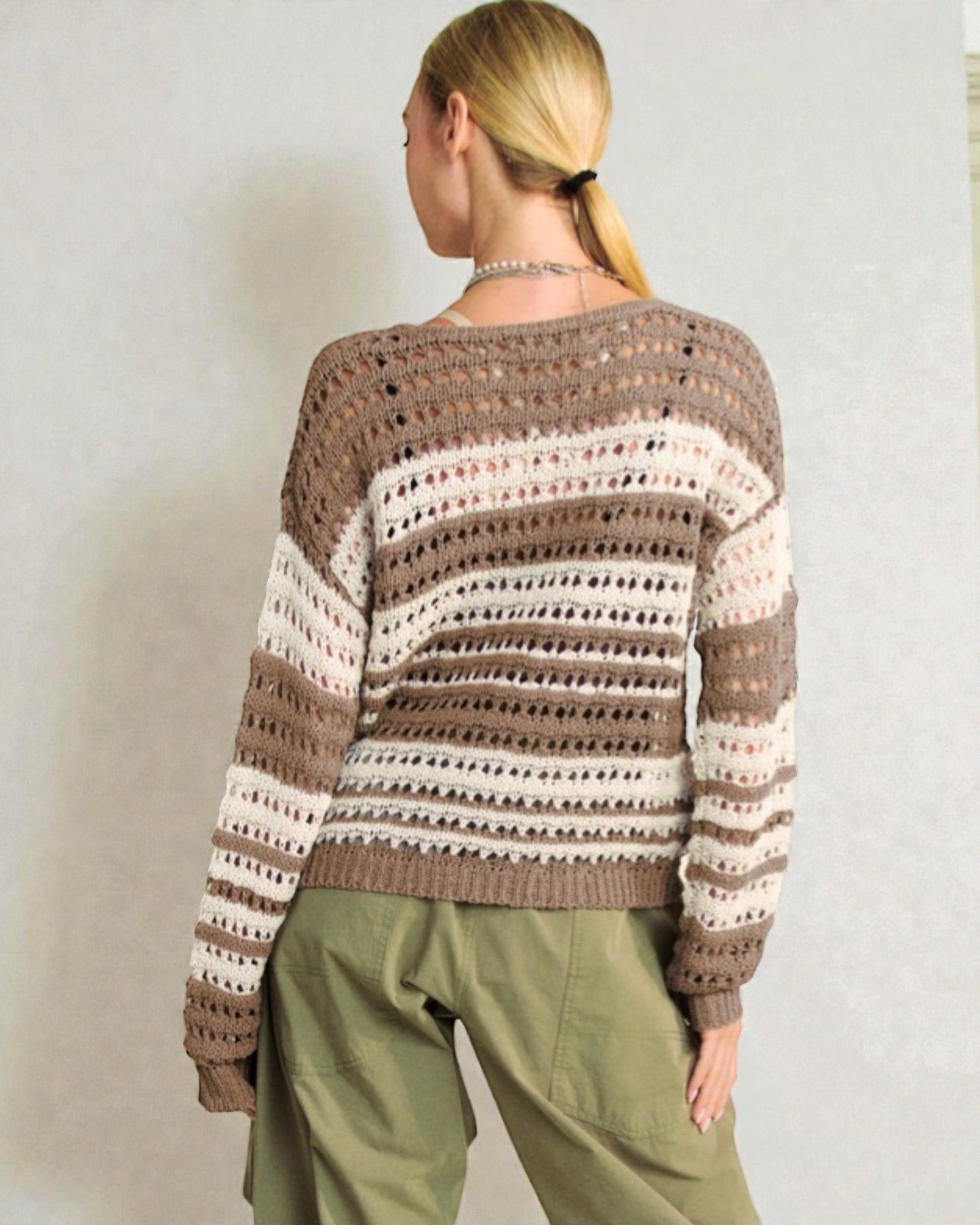 Person wearing a patterned sweater and green pants against a plain background