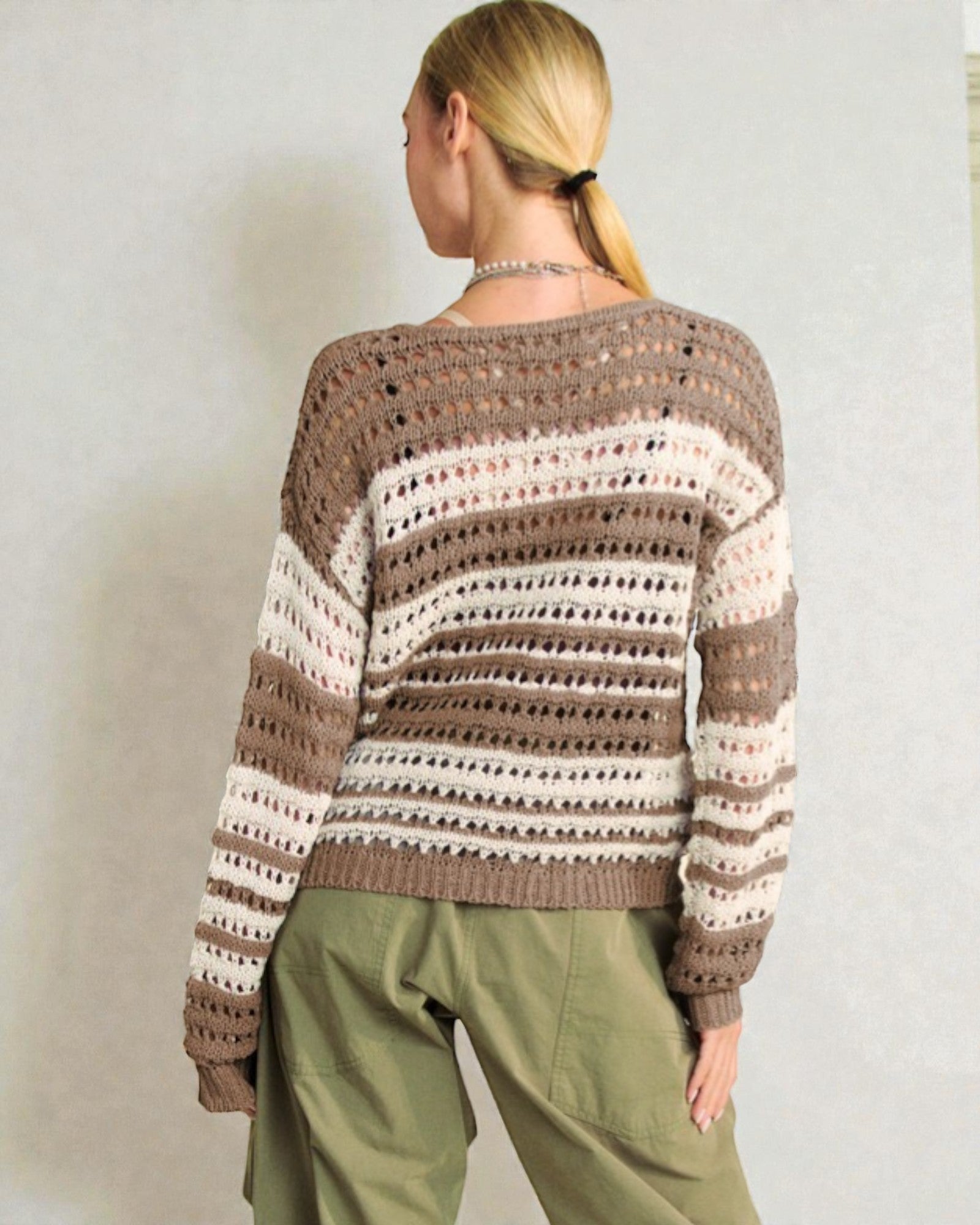 Person wearing a patterned sweater and green pants against a plain background