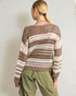 Person wearing a patterned sweater and green pants against a plain background