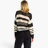 A woman viewed from behind wearing a black and cream striped knit sweater with a textured open-knit pattern, paired with black pants, against a plain white background.