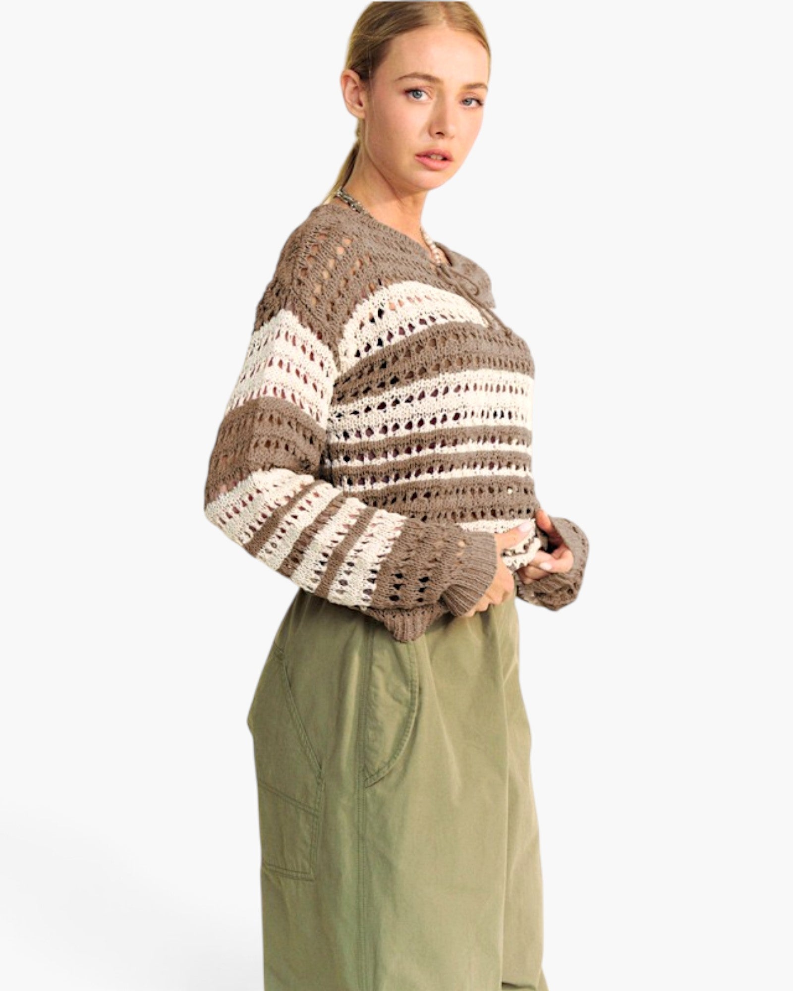 A woman wearing a brown and cream striped crochet knit sweater and olive green pants, photographed against a plain white studio background.