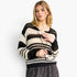 A woman modeling a black and cream crochet knit cardigan sweater with a drawstring, paired with a dark patterned skirt, against a plain white background.