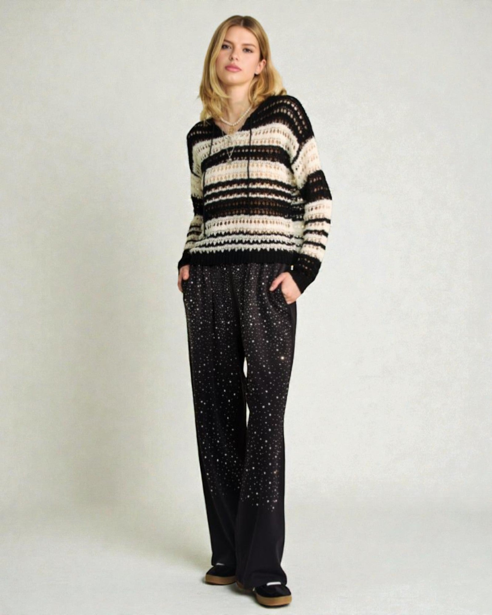 Woman wearing a black and white striped sweater and black pants with white patterns on a plain background