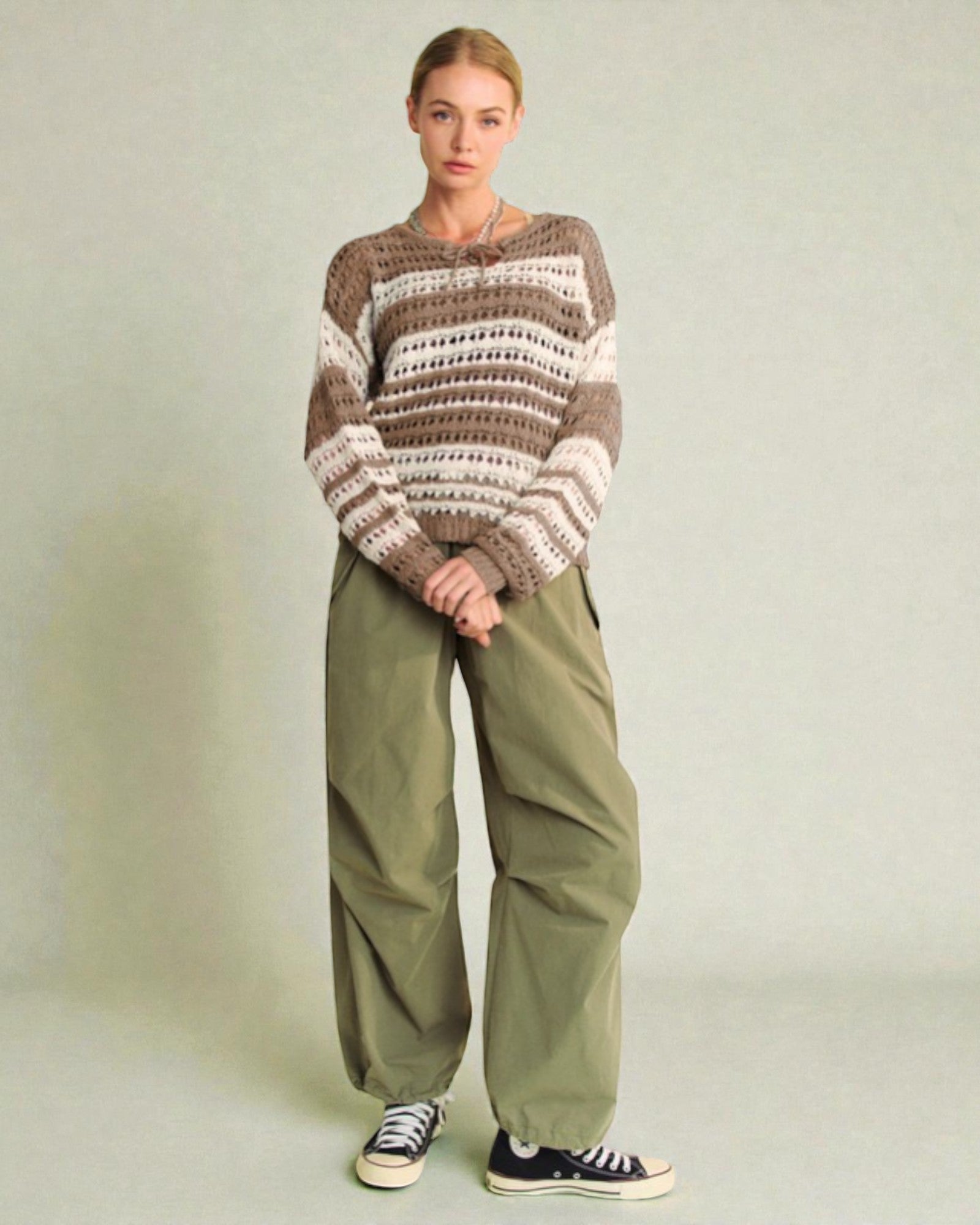 Person wearing a striped sweater and green pants on a plain background