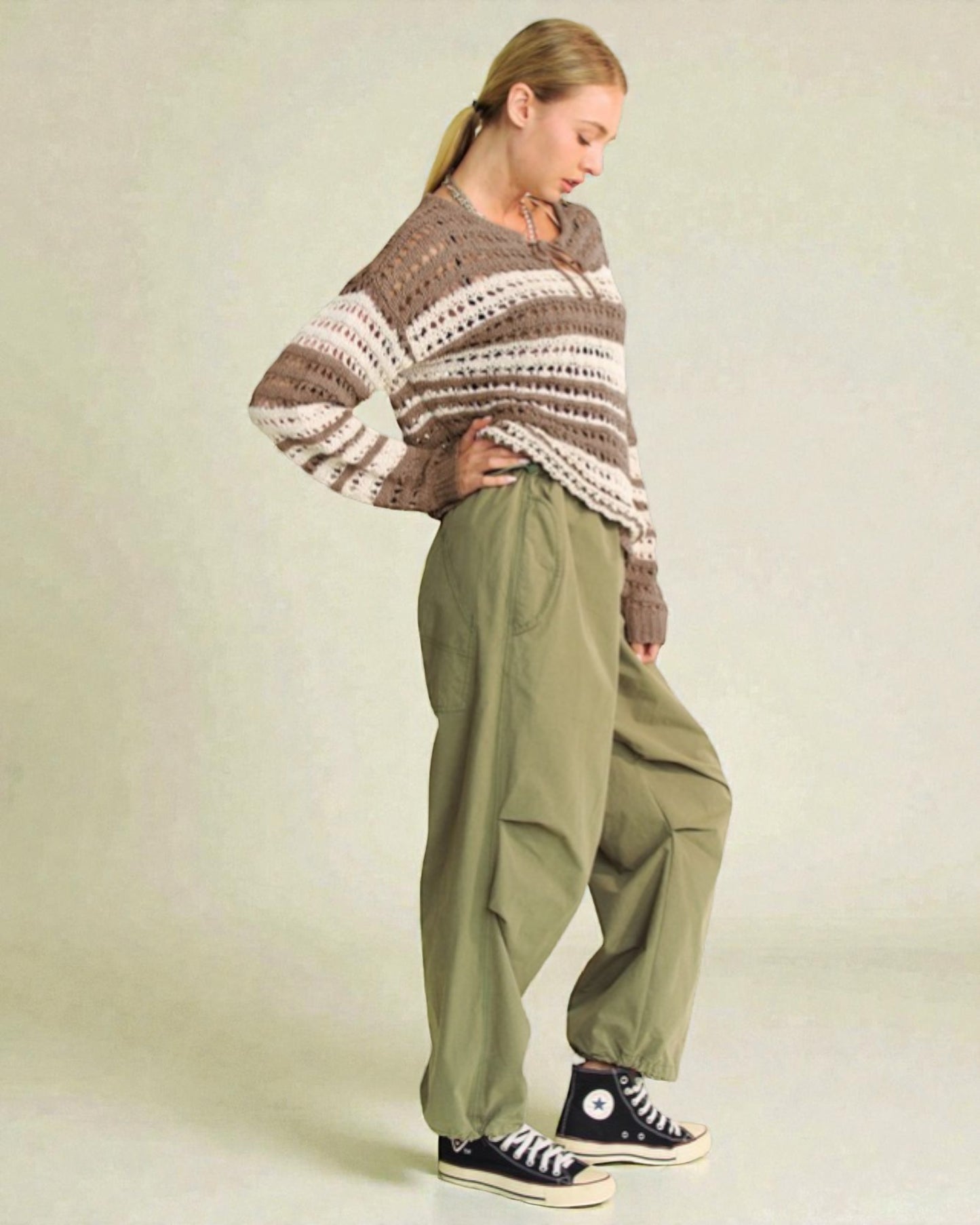 Person wearing a patterned sweater and green pants on a plain background