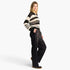 A woman modeling a black and cream striped knit cardigan sweater paired with black wide-leg pants featuring a sheer black mesh panel on the side, set against a plain white studio background.