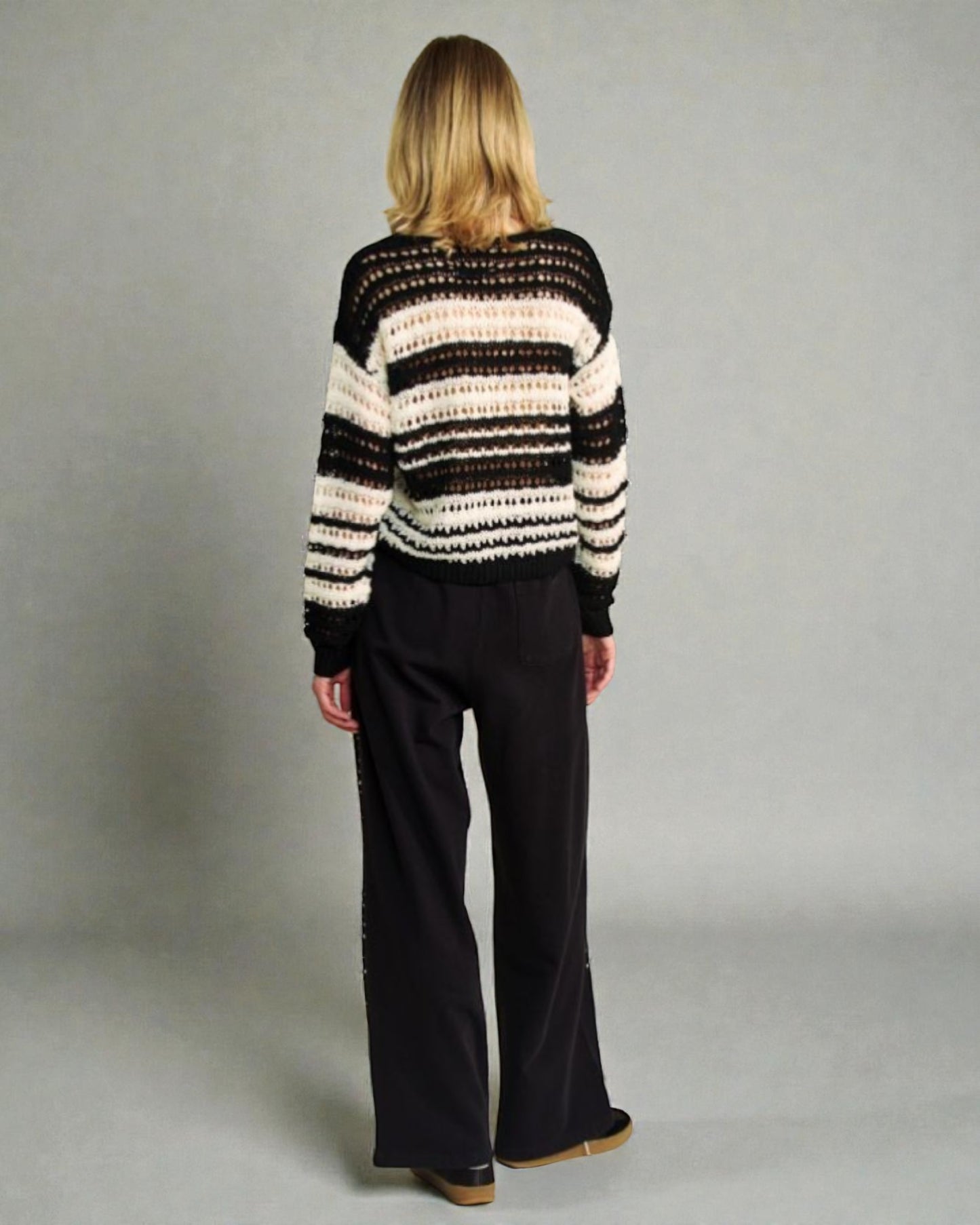 Person wearing a striped sweater and black pants against a plain background