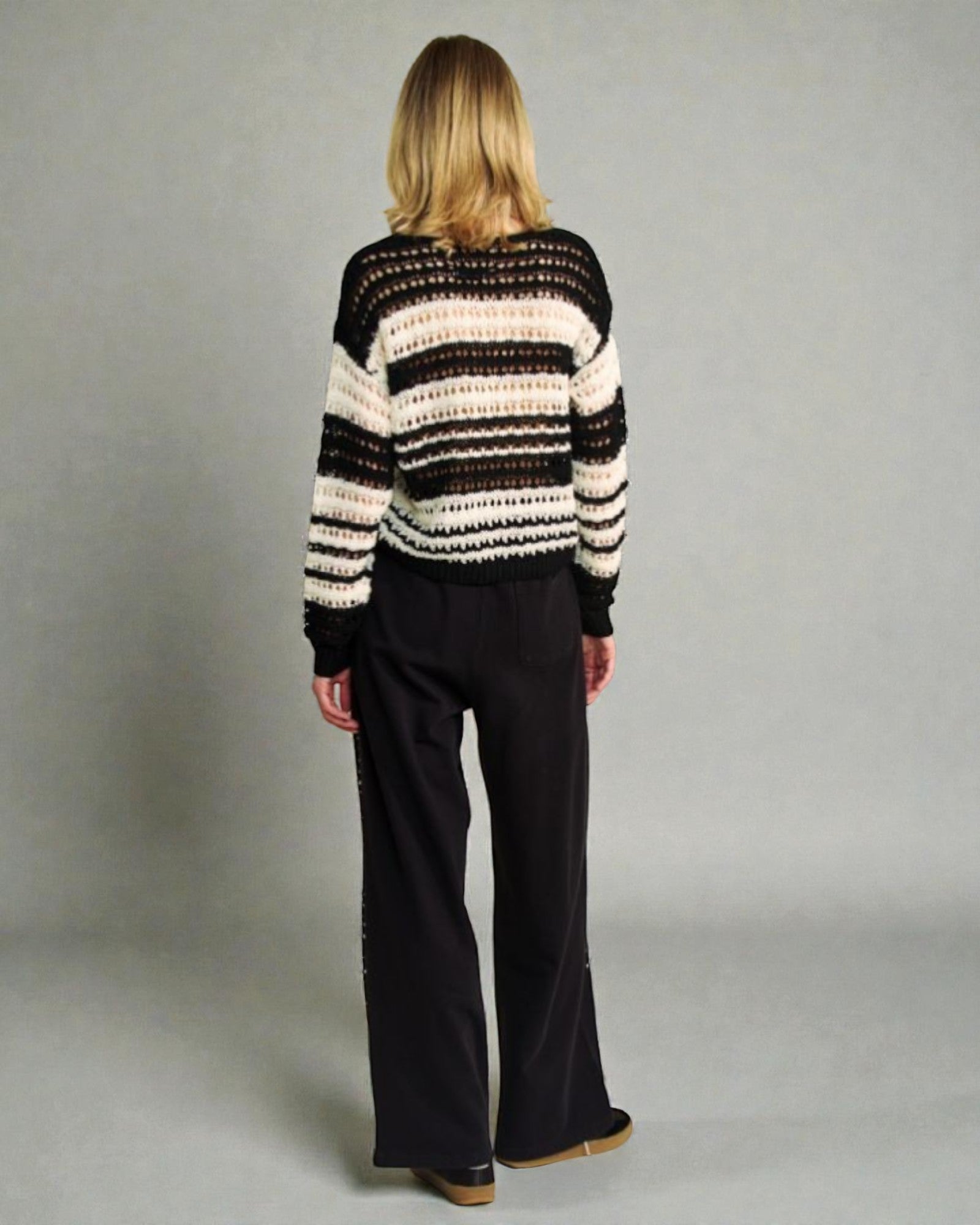Person wearing a striped sweater and black pants against a plain background
