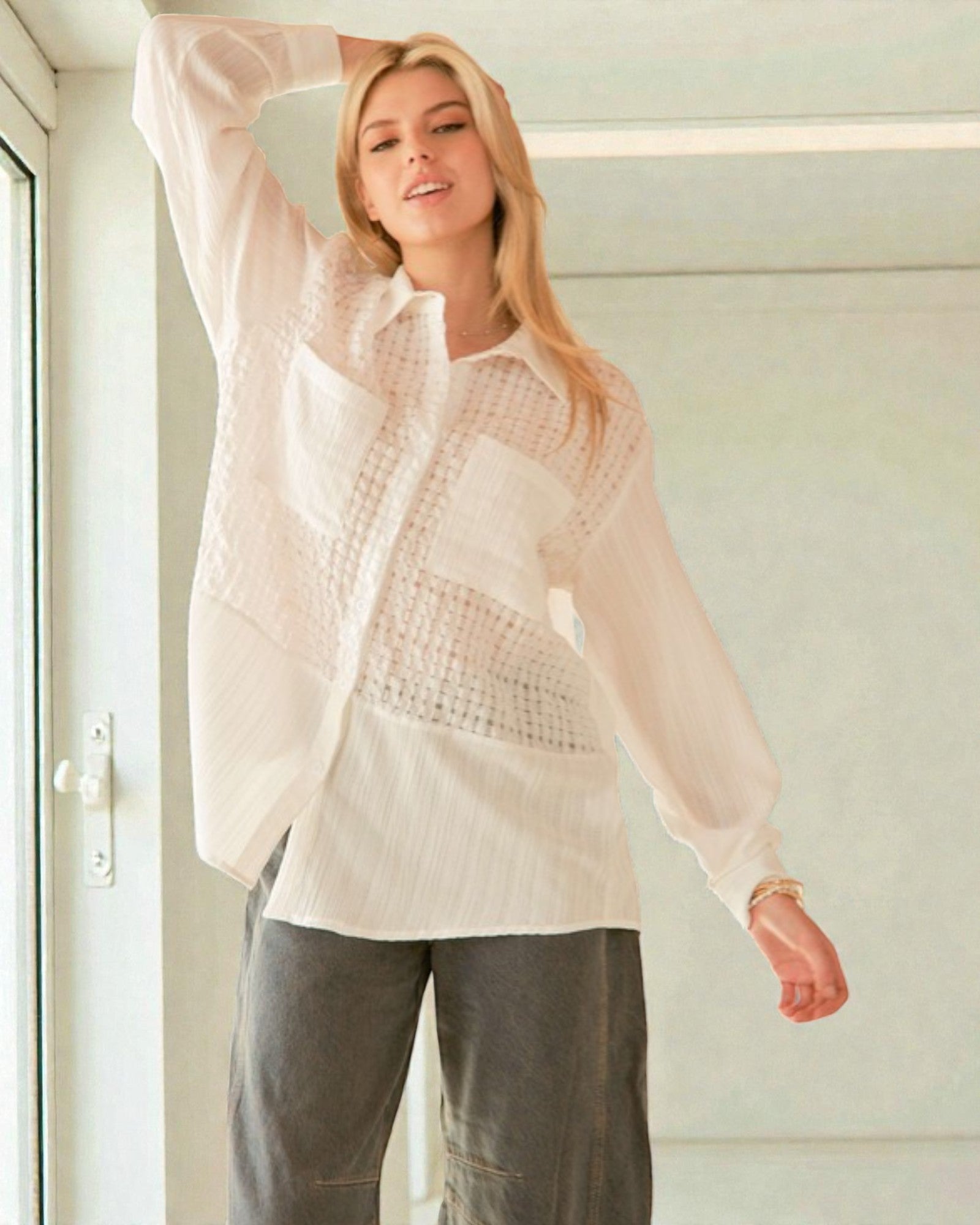 Woman wearing a light pink blouse and gray pants indoors.