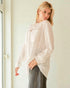 Woman wearing a light pink blouse with a textured pattern in a minimal indoor setting.