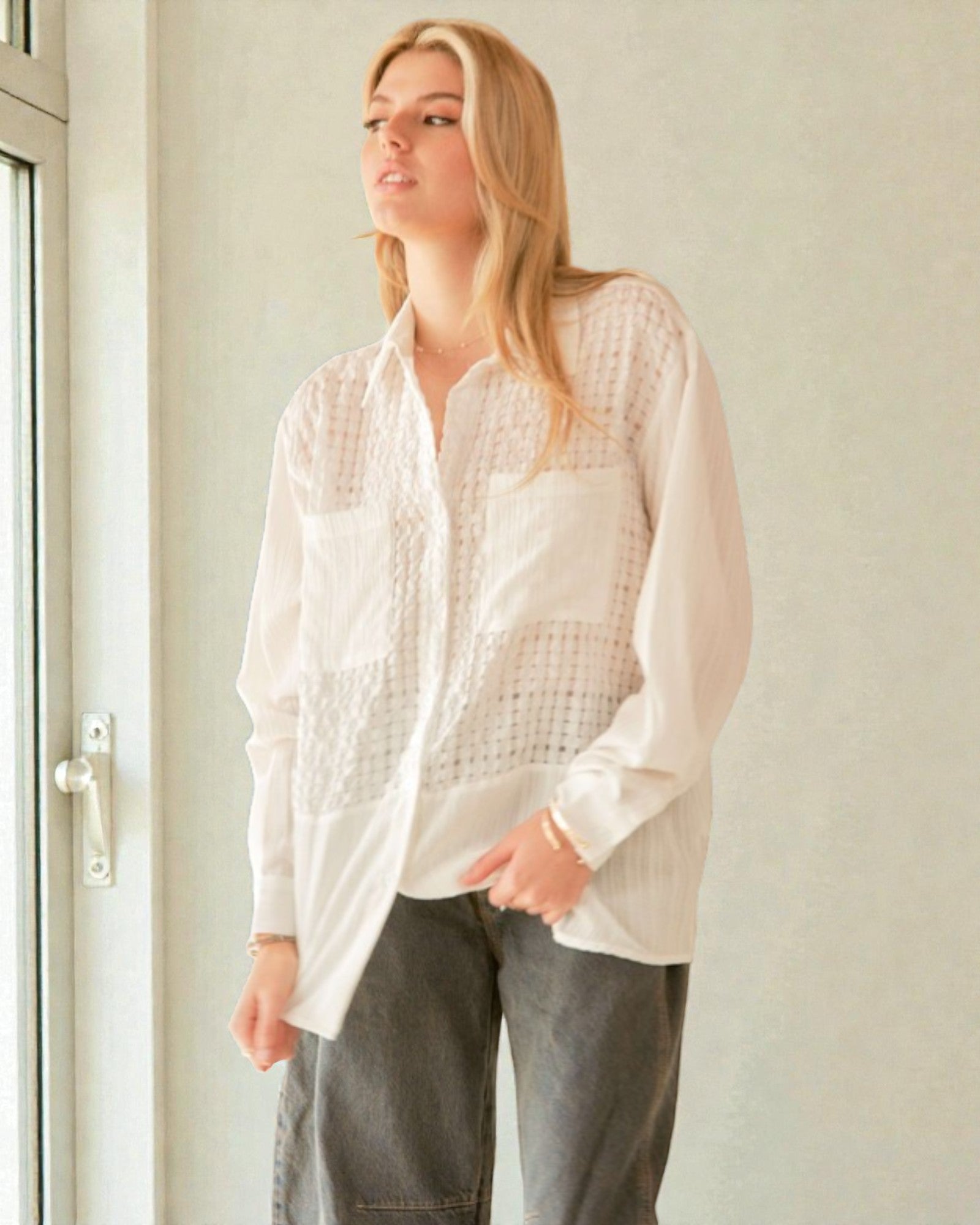 Woman wearing a white textured shirt and gray pants standing indoors.
