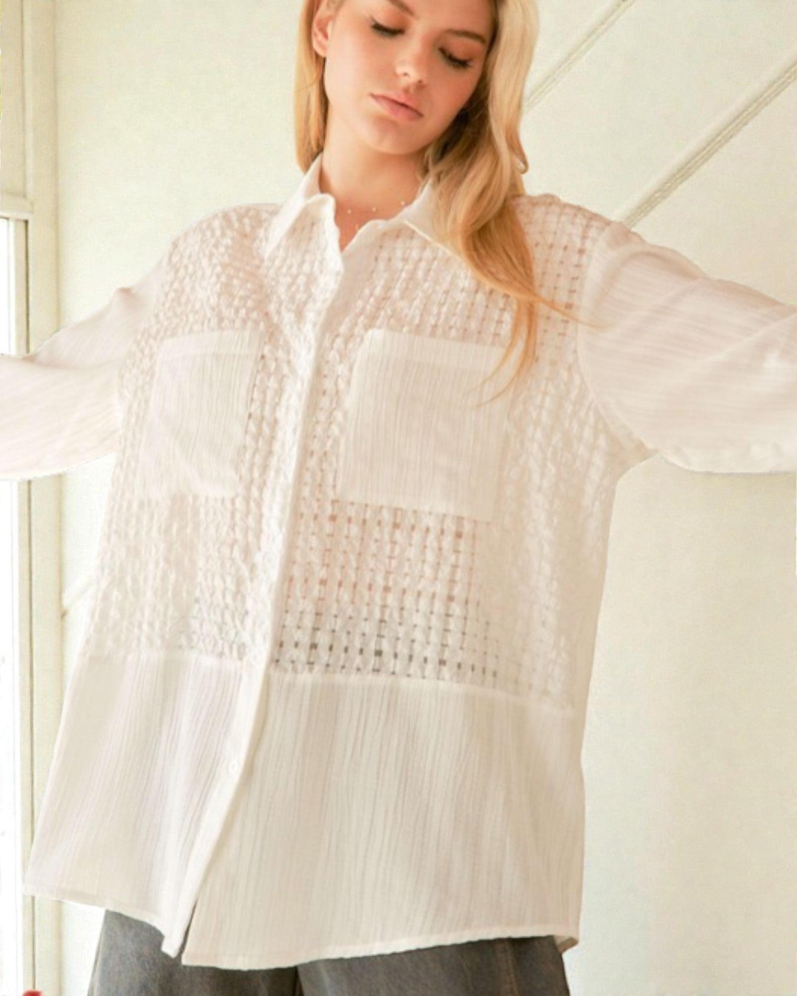 Woman wearing a white textured shirt with arms outstretched indoors.