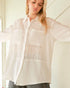 Woman wearing a white textured shirt with arms outstretched indoors.