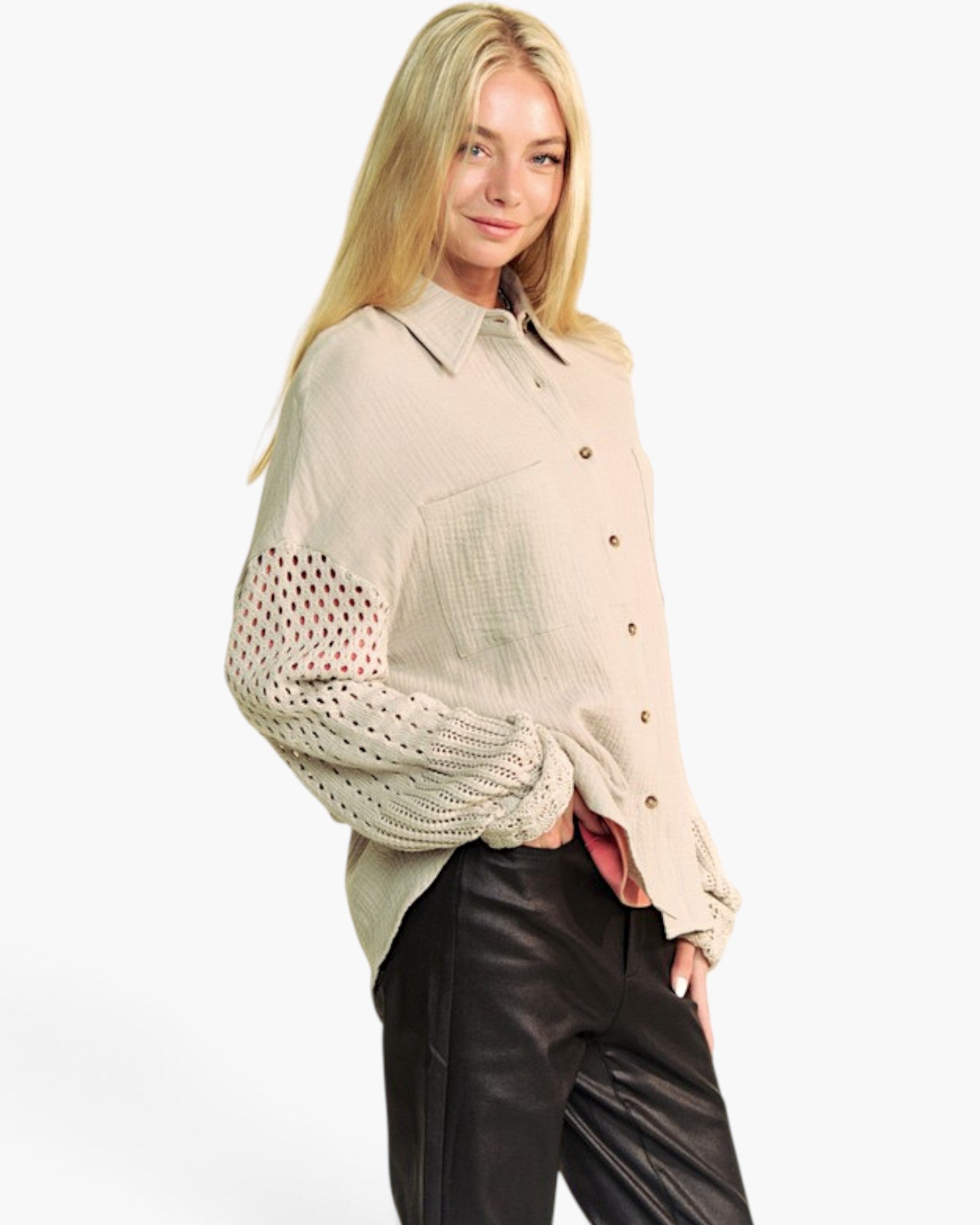 A woman modeling a light beige textured button-up shirt with sheer, open-knit elbow patches on the sleeves, paired with black leather pants against a plain white background.