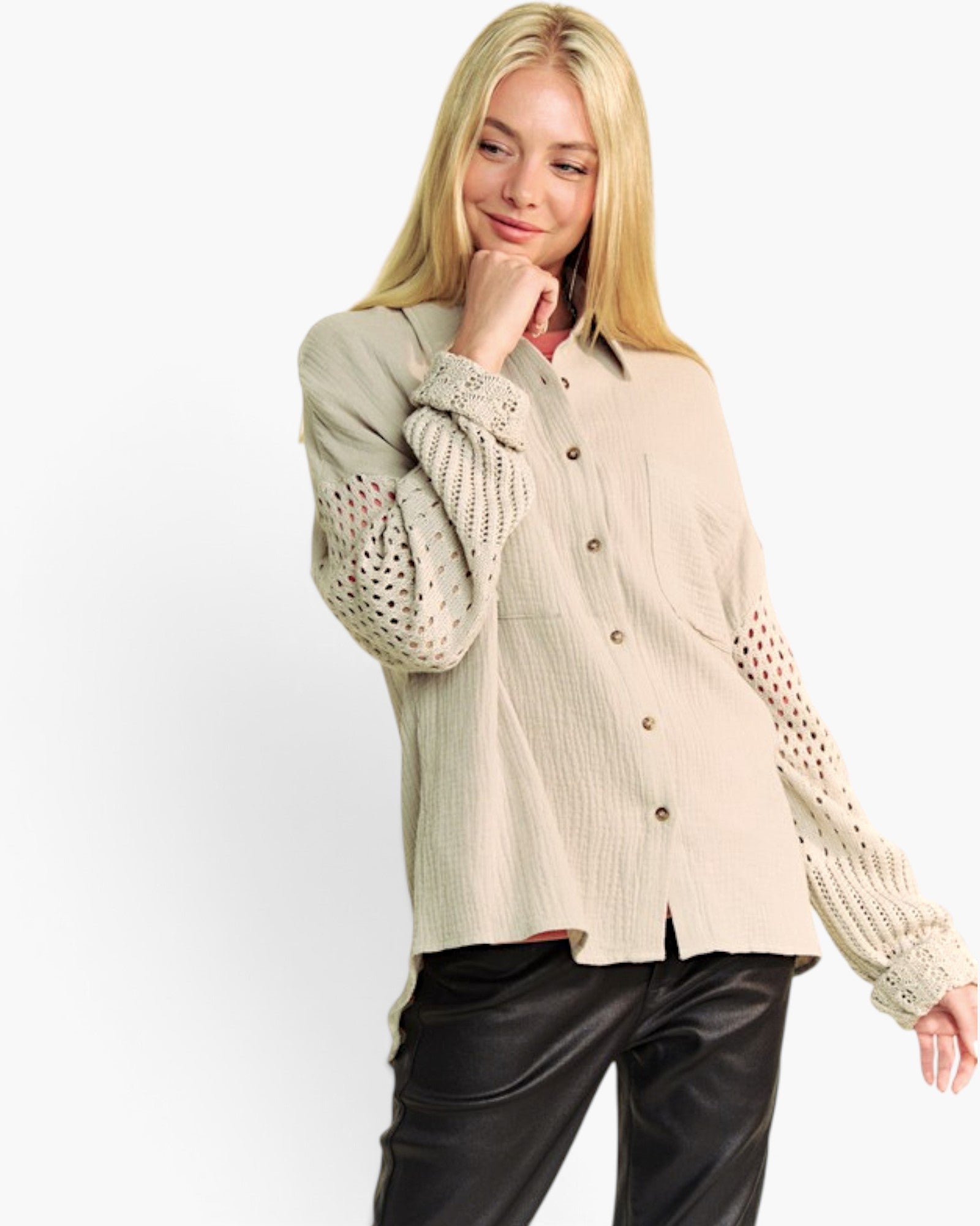 A blonde woman wearing a beige textured button-up shirt with openwork knit sleeves and black pants, posing against a plain white studio background.