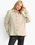 A woman modeling a light beige textured button-up shirt with knit cowl sleeves and black leather pants, photographed against a clean white studio background.