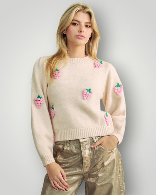 Woman wearing a light pink sweater with embroidered designs on a plain background