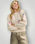 Woman wearing a cream sweater with pink berry designs on a plain background