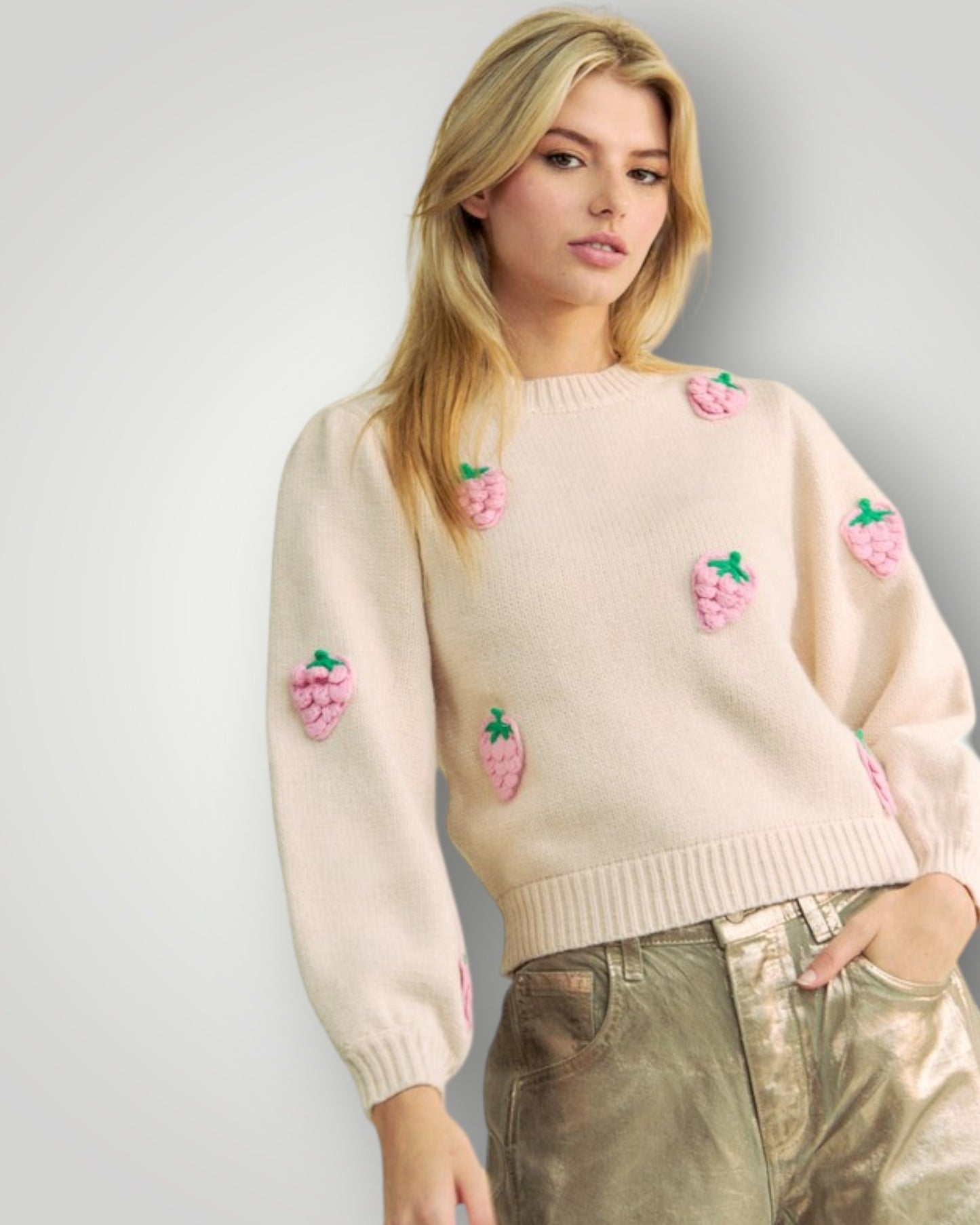 Woman wearing a cream sweater with pink floral embellishments against a plain background