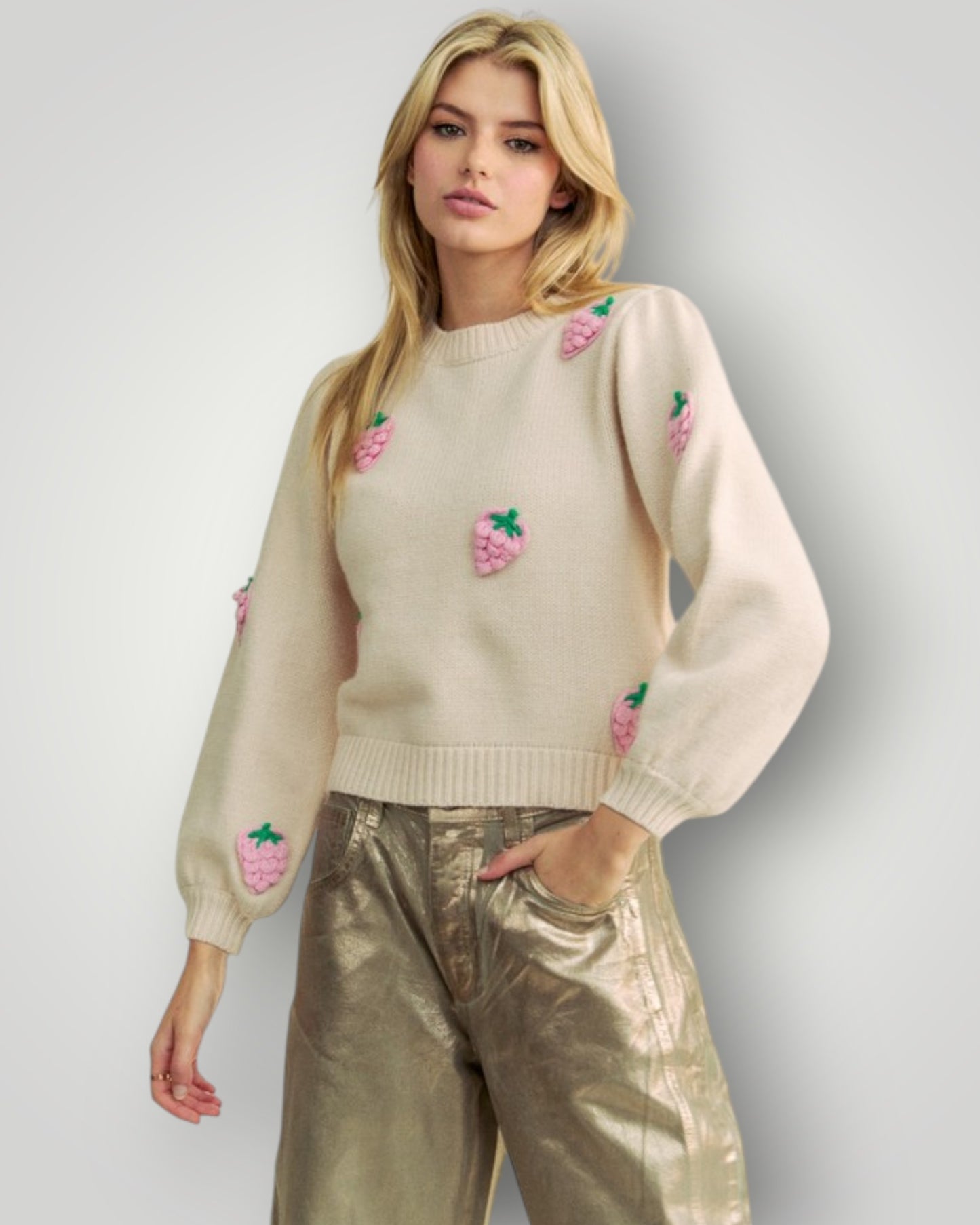 Woman wearing a beige sweater with floral embroidery and gold pants on a light gray background