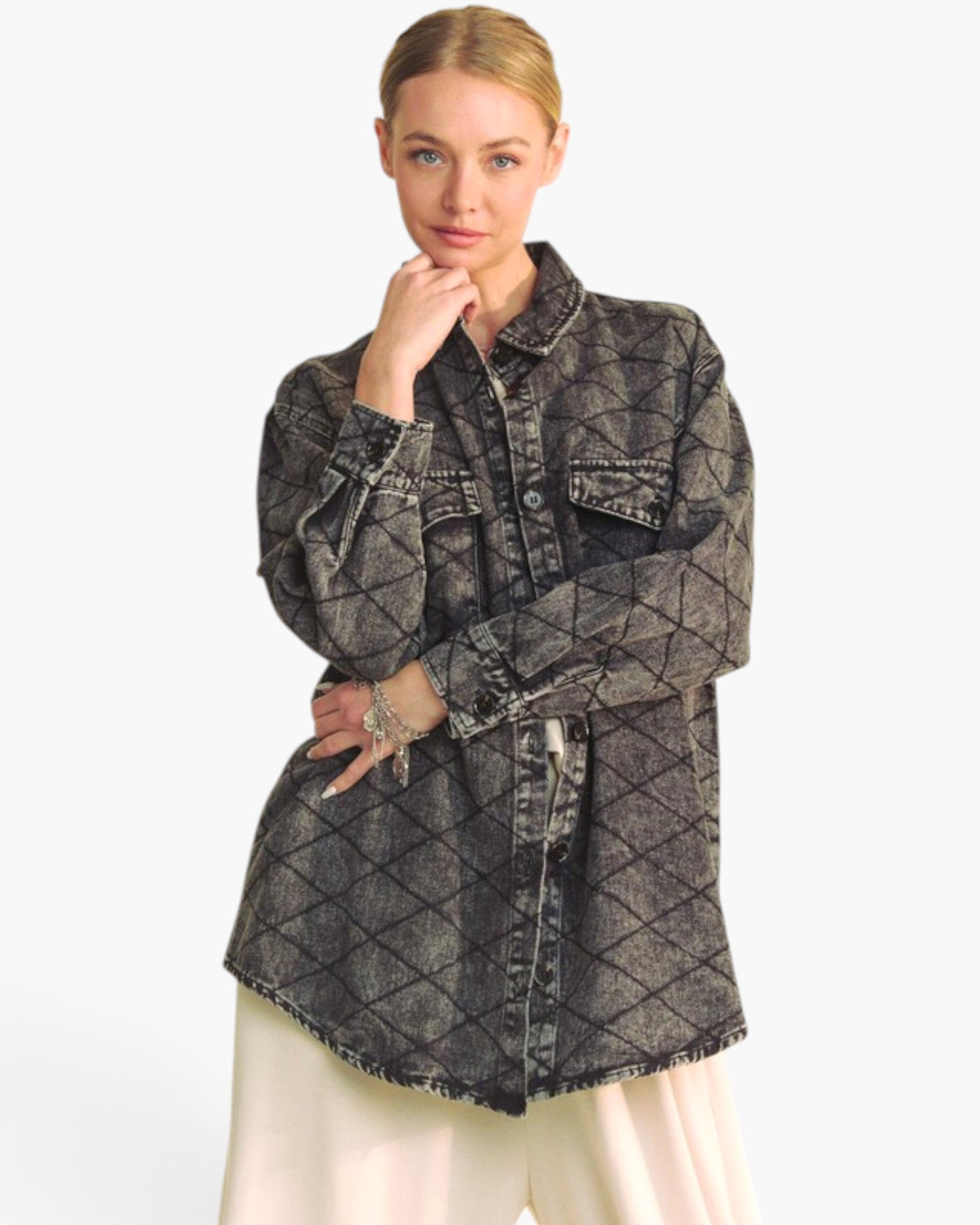 A woman modeling a dark gray washed denim shirt jacket with a black diamond grid pattern, paired with cream-colored pants, against a plain white studio background.