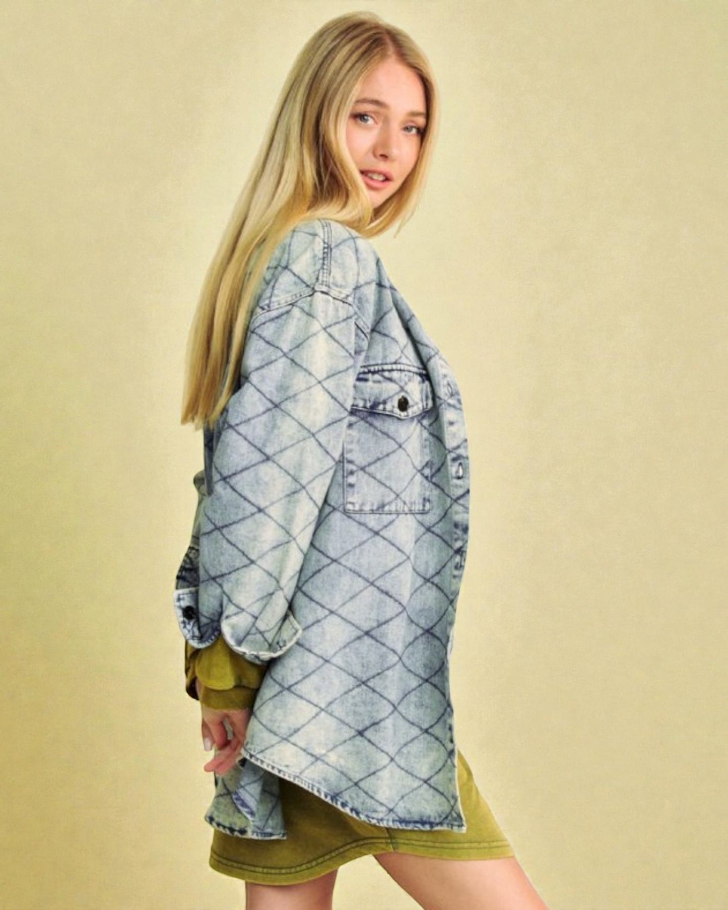 Woman wearing a light blue denim jacket over a green dress on a beige background