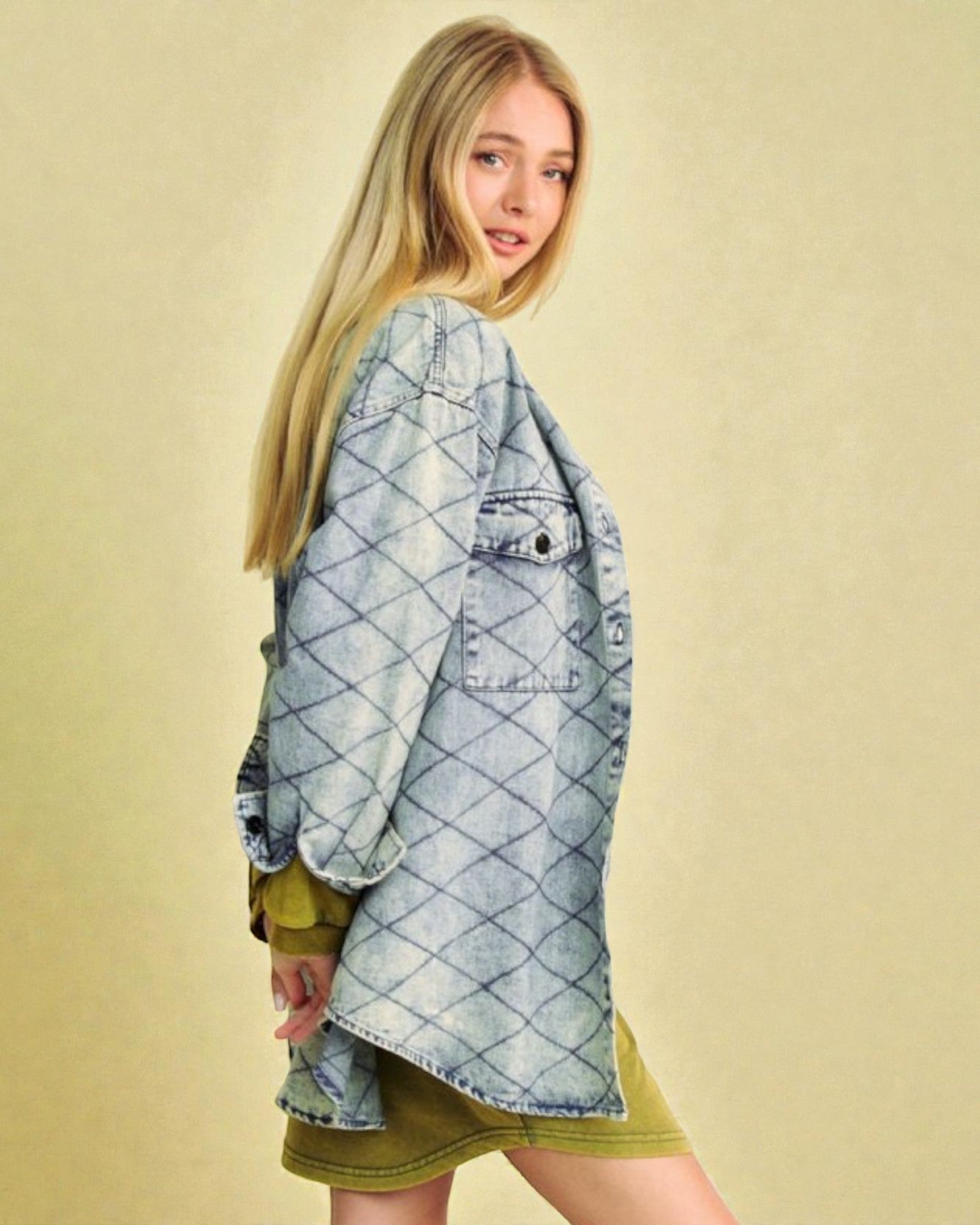 Woman wearing a light blue denim jacket over a green dress on a beige background