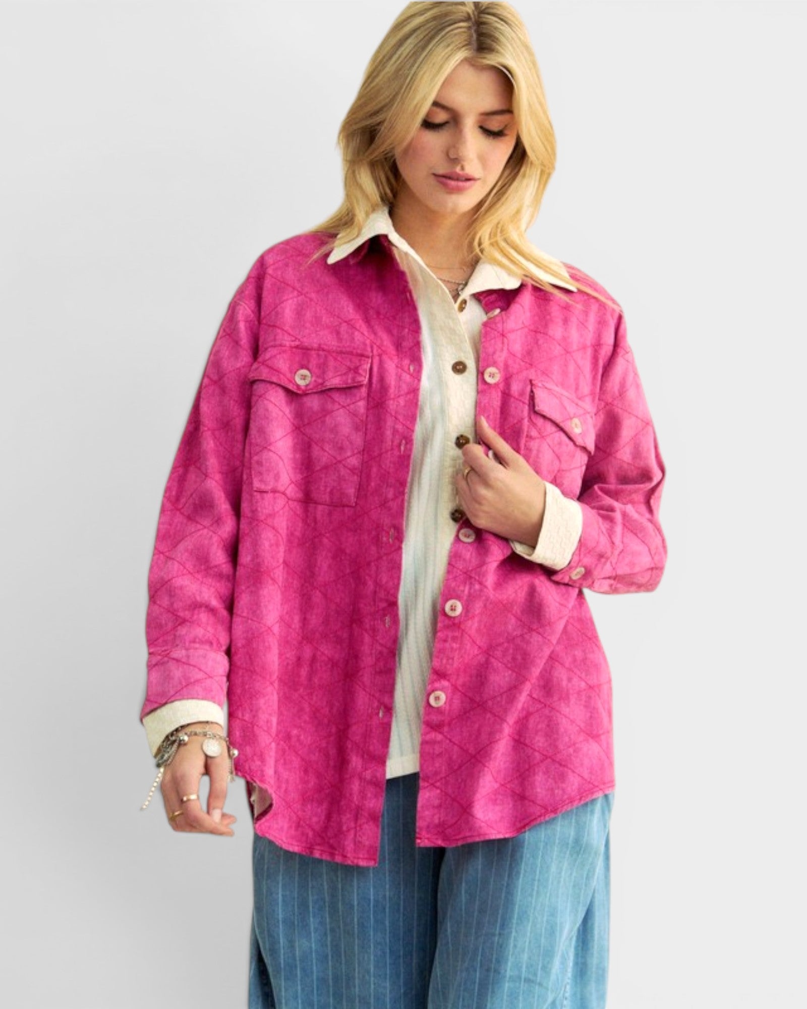Woman wearing a bright pink shirt over a white collared shirt with blue jeans on a light gray background