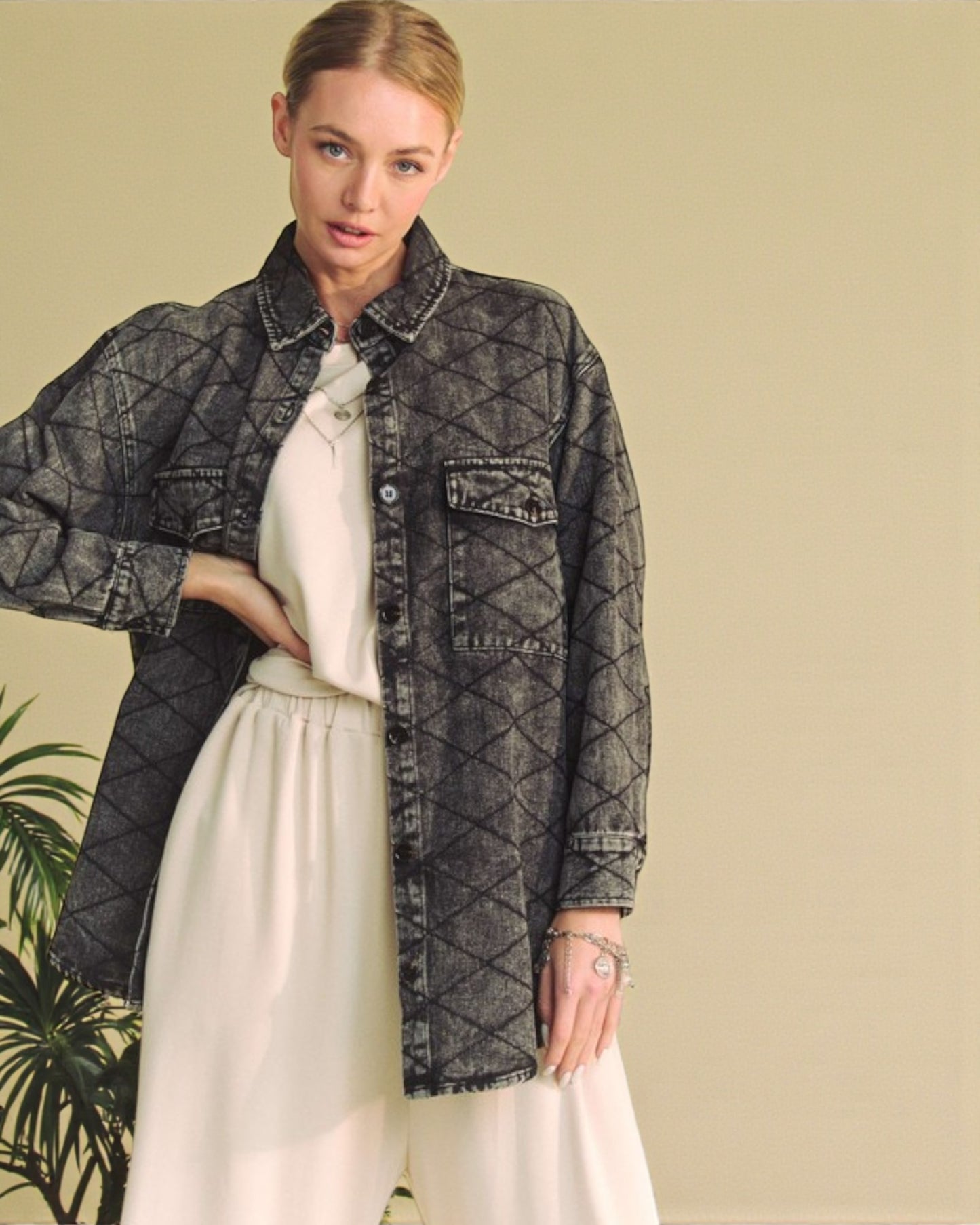 Woman wearing a dark denim jacket over a white shirt and pants against a beige background