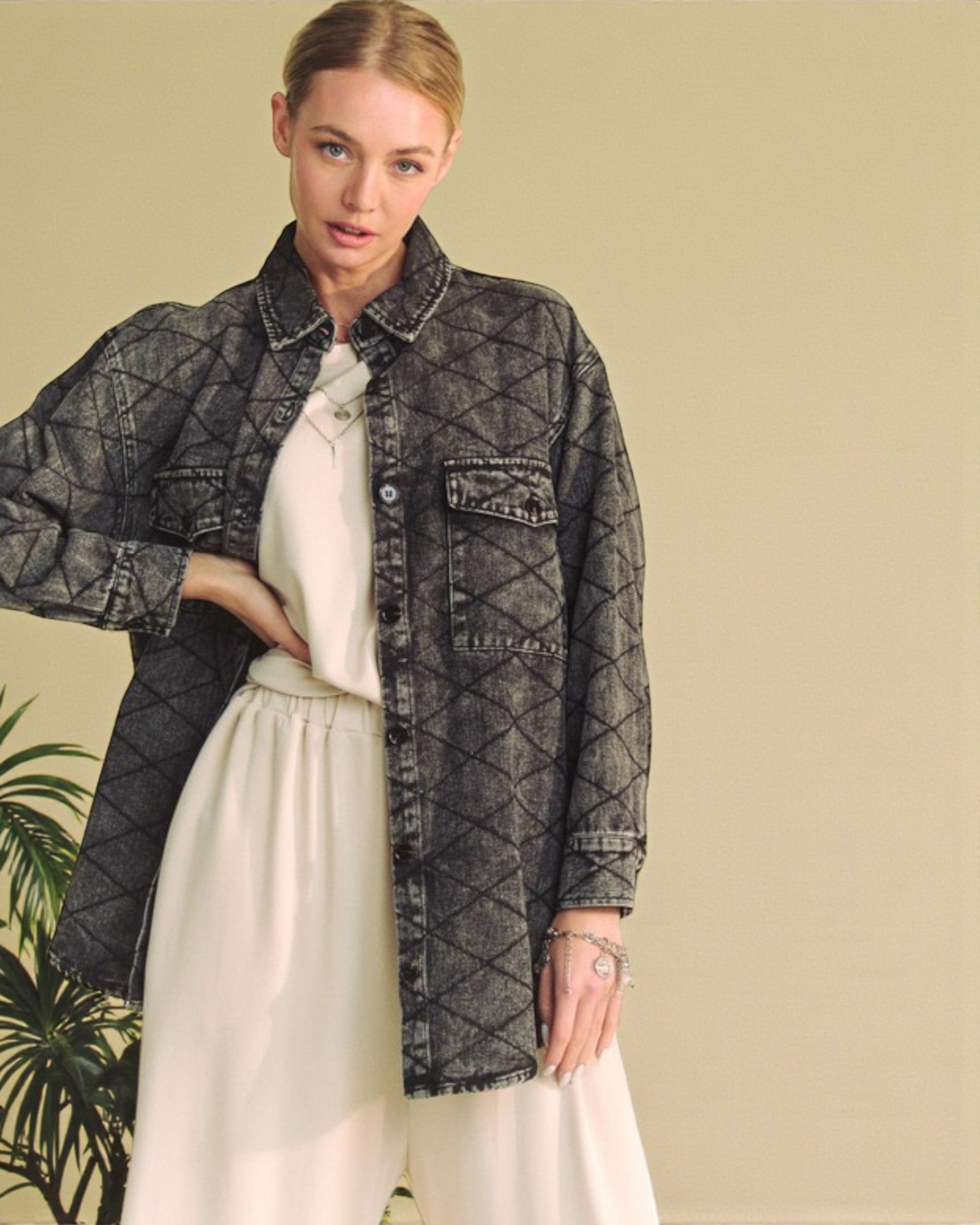 Woman wearing a dark denim jacket over a white shirt and pants against a beige background