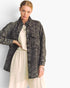 A woman models a dark gray quilted denim jacket over a cream-colored top and wide-leg trousers, set against a plain light gray studio background.