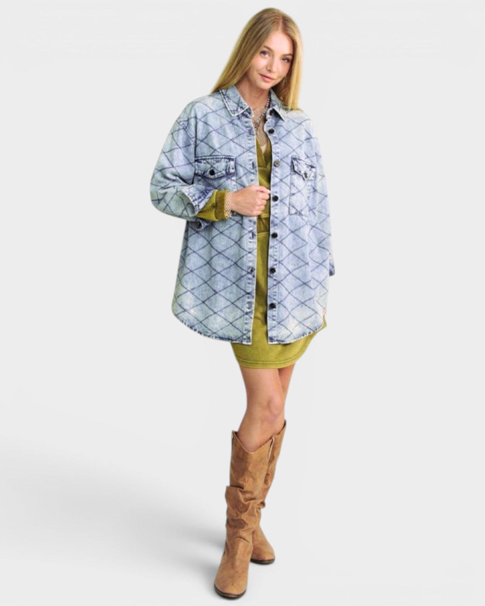 Woman wearing a denim jacket over a green dress with brown boots on a white background