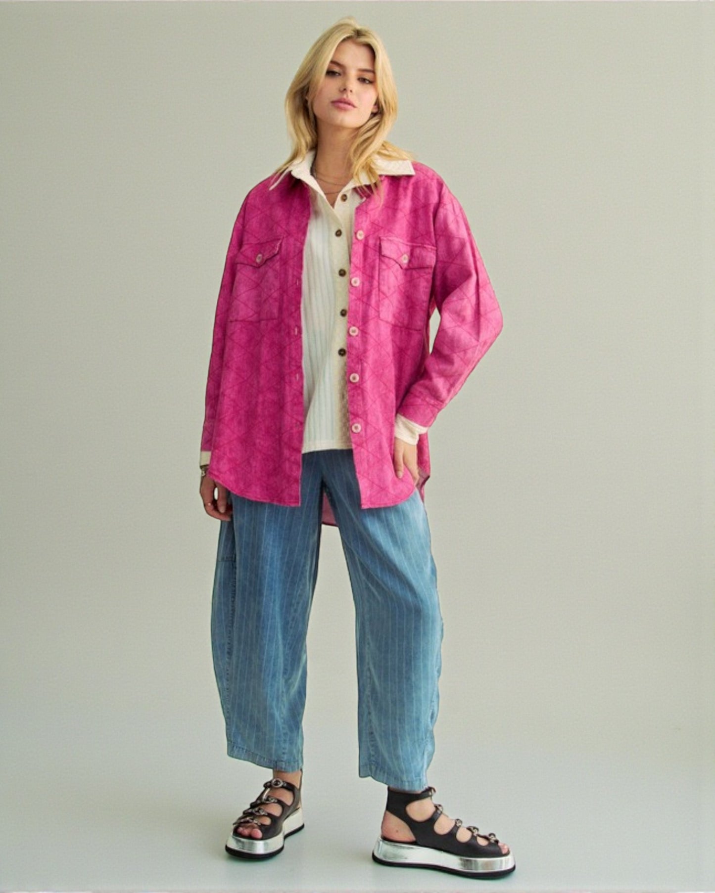 Woman wearing a pink jacket over a white shirt with blue jeans on a plain background