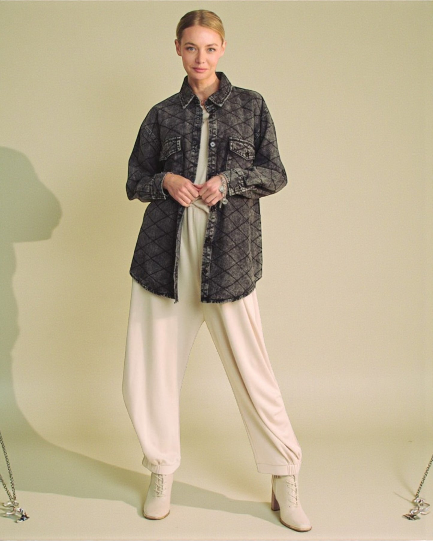 Woman wearing a dark patterned shirt and light-colored pants against a plain background