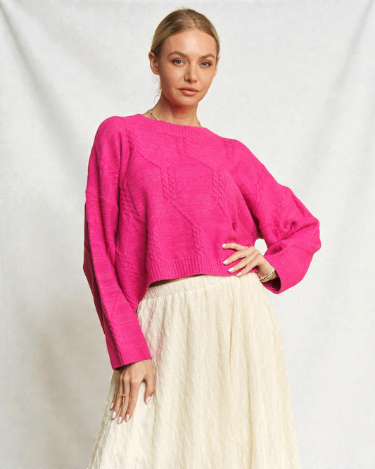 Woman wearing a bright pink sweater and white skirt against a plain background