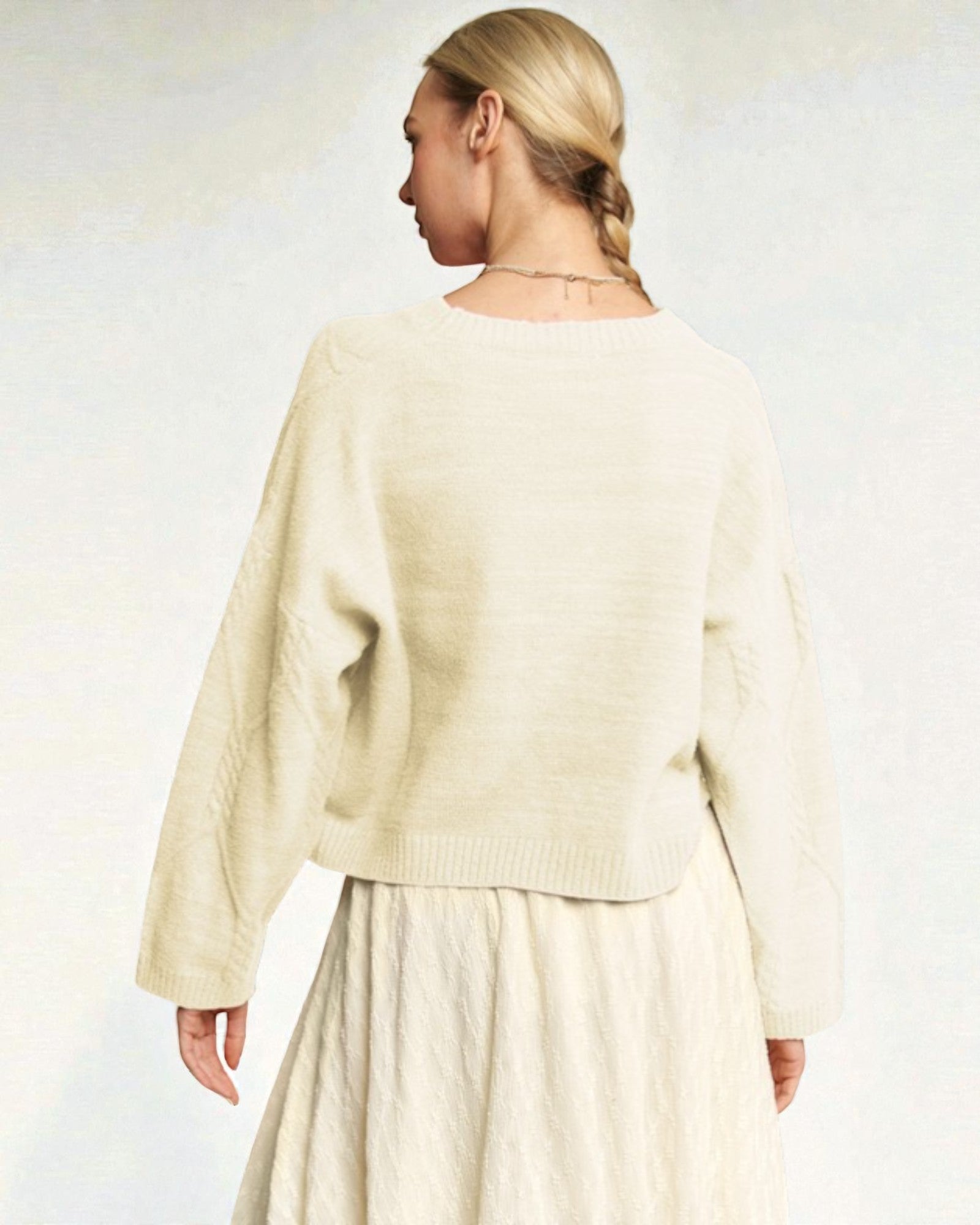 Person wearing a light-colored sweater and skirt set on a plain background