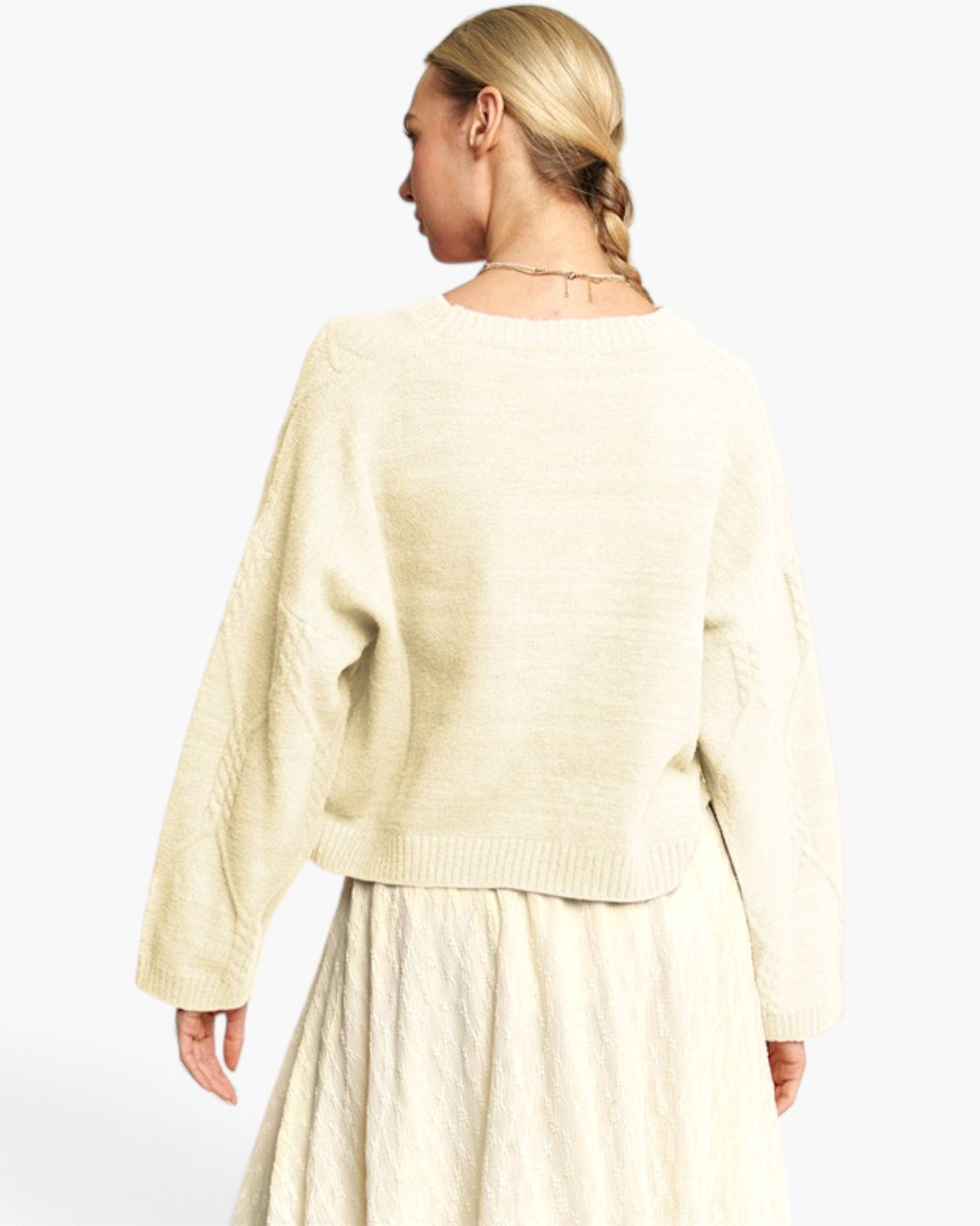 A woman shown from the back wearing a cream-colored knit sweater and matching skirt against a plain white studio background.