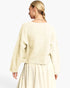 A woman shown from the back wearing a cream-colored knit sweater and matching skirt against a plain white studio background.