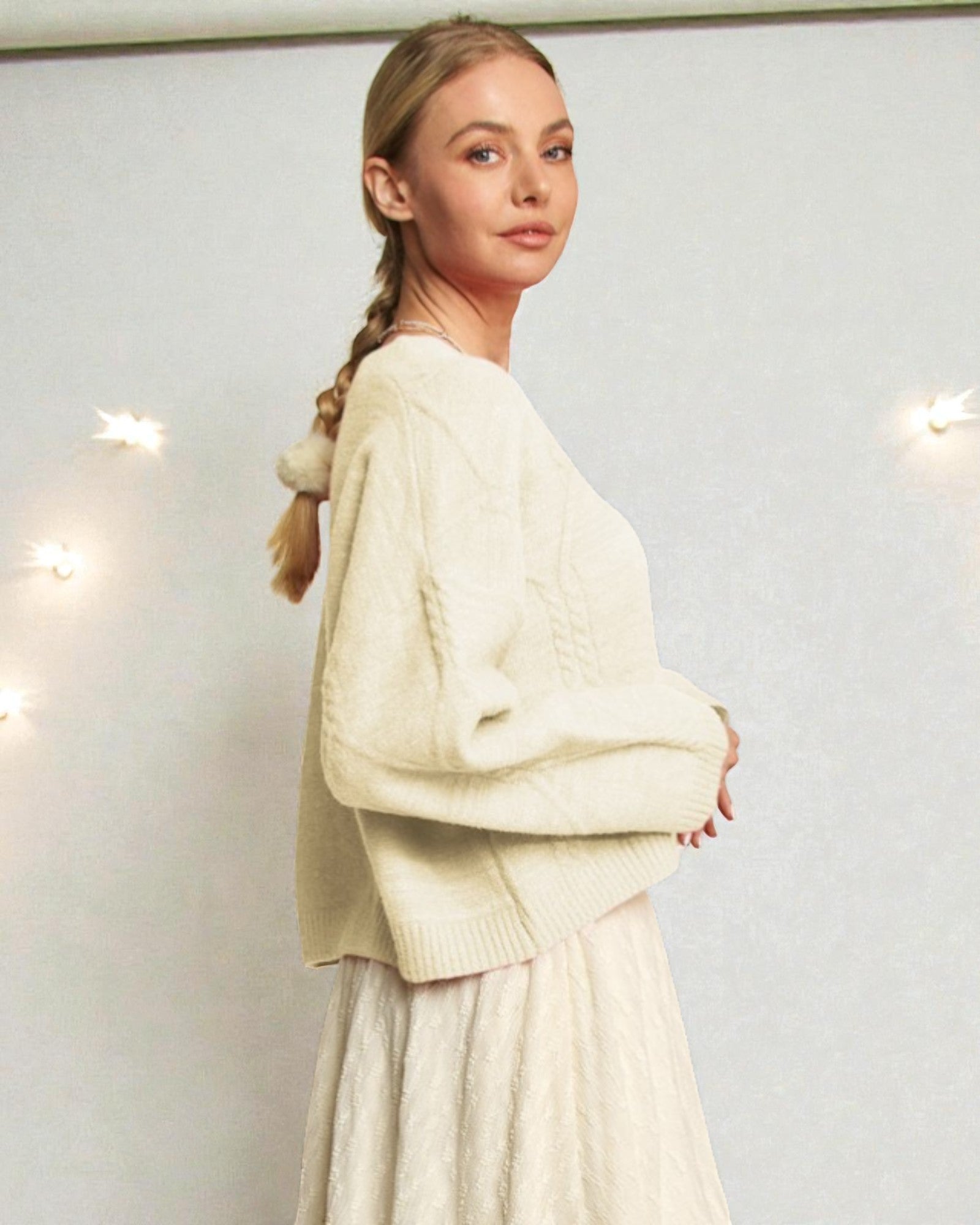 Woman wearing a cream-colored sweater and skirt set against a light background