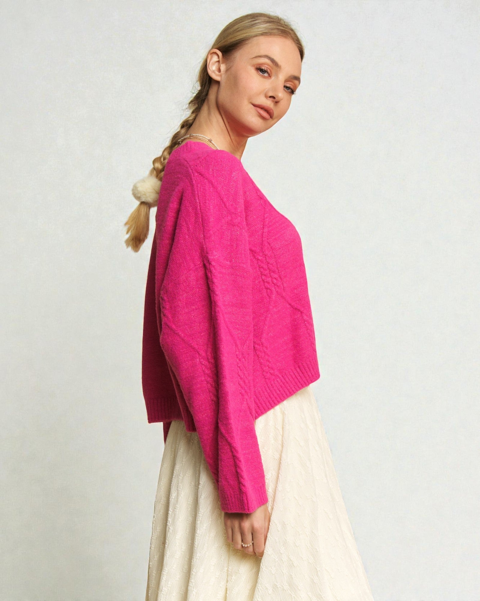 Woman wearing a bright pink sweater and white pants on a plain background