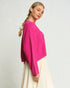 Woman wearing a bright pink sweater and white pants on a plain background
